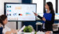 Young team leader in big corporation briefing coworkers pointing at graph meeting. Corporate staff discussing new business application with colleagues looking at screen