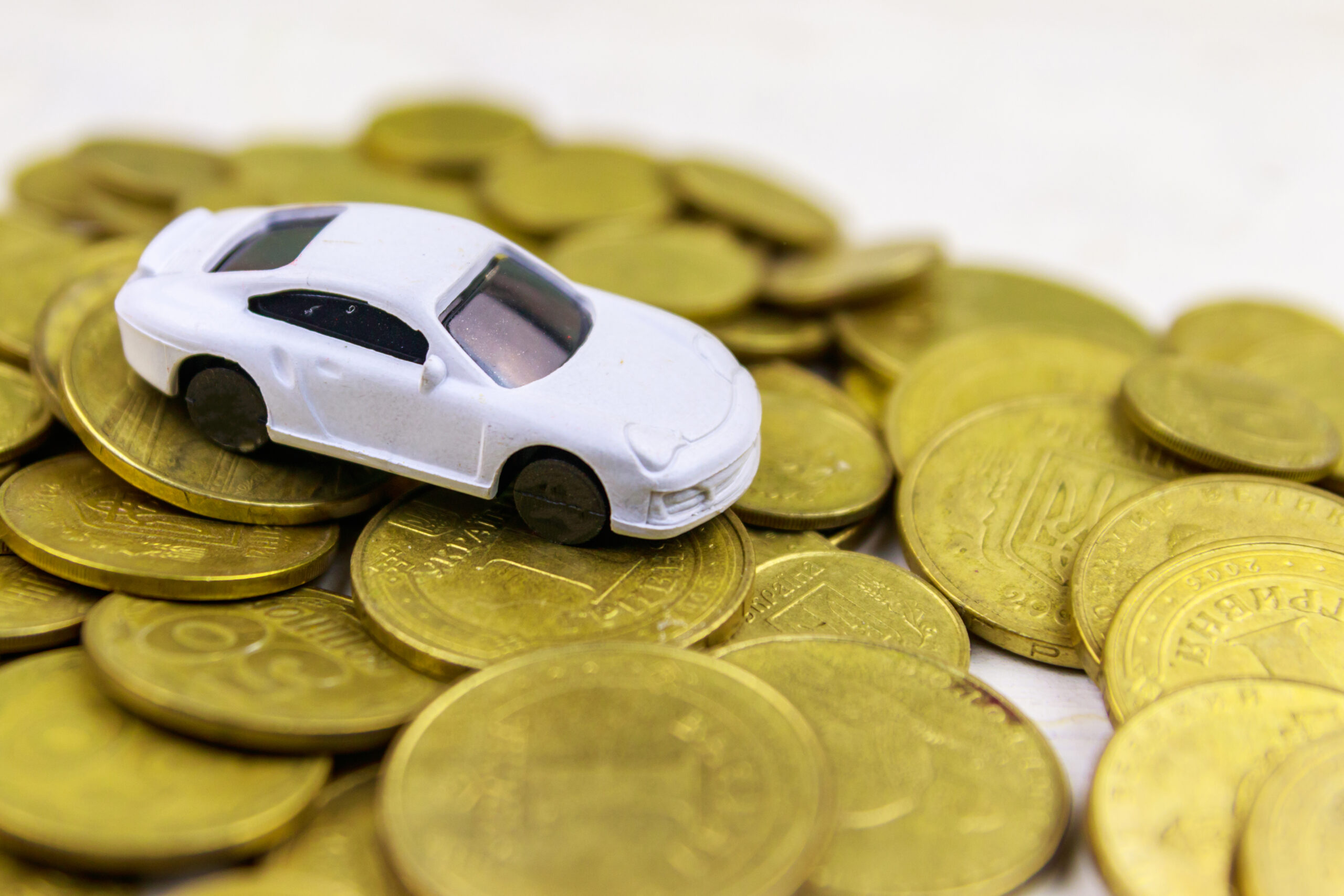 Miniature car model on heap of golden coins on white wooden bac